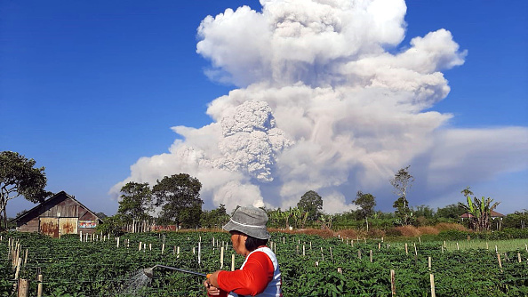 -Un agriculteur travaille dans sa ferme alors que le mont Sinabung crache des cendres dans le ciel, vu de Karo, au nord de Sumatra, le 2 mars 2021. Photo par Bahari Tarigan / AFP via Getty Images.