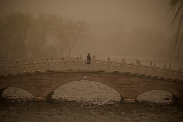 -Une femme traverse un pont au lac Houhai lors d'une tempête de sable à Pékin le 15 mars 2021. Photo de Noel Celis / AFP via Getty Images.