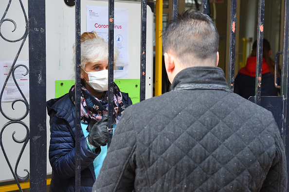 Une enseignante d'une école primaire, portant un masque de protection, parle à un parent à Bordeaux, le 17 mars 2020, quelques heures avant l'entrée en vigueur des mesures de confinement pour tous les citoyens français. (NICOLAS TUCAT/AFP via Getty Images)