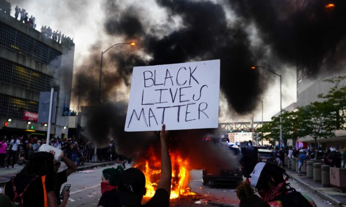 Un homme brandit une pancarte de Black Lives Matter alors qu'une voiture de police brûle lors d'une manifestation à Atlanta, Géorgie, le 29 mai 2020. (Elijah Nouvelage/Getty Images)