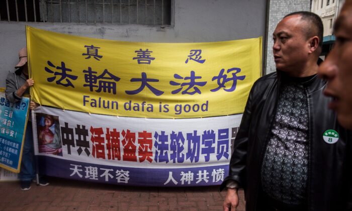Une pratiquante de Falun Gong (G) tient une pancarte à côté d'un groupe de touristes (D) de Chine continentale dans le quartier de Kowloon à Hong Kong, le 6 janvier 2019. (Isaac Lawrence/AFP via Getty Images)