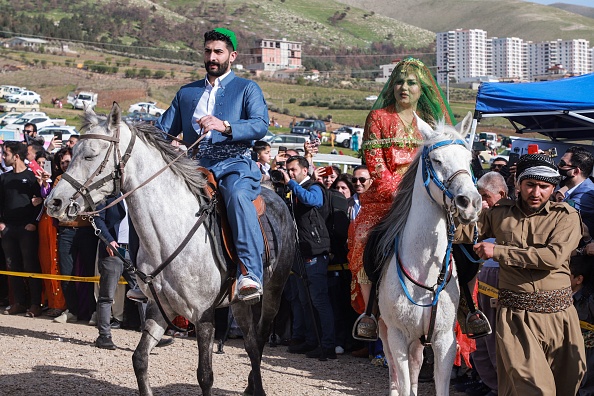 -Un homme et une femme vêtus de vêtements traditionnels montent à cheval lors d'une célébration kurde irakienne du Nouvel An persan, au Kurdistan irakien, le 20 mars 2021. Photo par Shwan MOHAMMED / AFP via Getty Images.