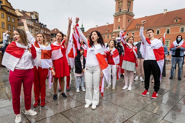 Des manifestants lèvent la main portant un drapeau biélorusse traditionnel, symbole de l'opposition, alors que les Biélorusses vivant en Pologne et les Polonais participent à une manifestation réclamant la liberté du militant de l'opposition biélorusse Roman Protasevich, sur la place du château à Varsovie, Pologne, le 29 mai 2021. (Photo : WOJTEK RADWANSKI/AFP via Getty Images)