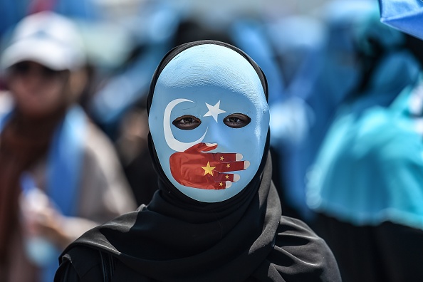 Manifestant portant un masque peint aux couleurs du drapeau du Turkestan oriental et une main portant les couleurs du drapeau chinois. (Photo : OZAN KOSE/AFP via Getty Images)