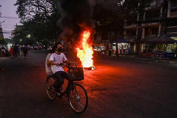 -Un couple à vélo devant une barricade de fortune en feu, érigée par des manifestants à Yangon, le 3 avril 2021. Photo par STR/AFP via Getty Images.