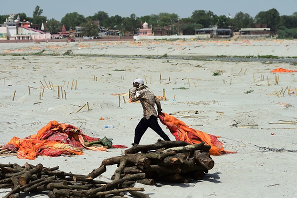 -Un ouvrier retire des tissus safran de cadavres enterrés dans le sable près d'un terrain de crémation sur les rives du Gange, le 24 mai 2021. Photo de SANJAY KANOJIA/AFP via Getty Images.