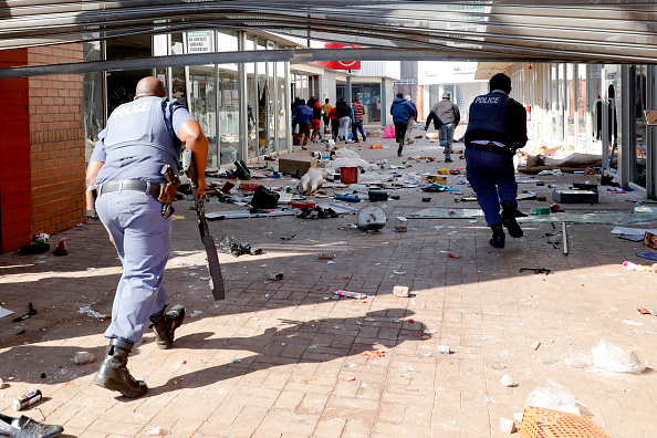 -Des gens fuient la police alors qu'ils transportent des marchandises tout en pillant et en vandalisant le centre commercial à l'est de Johannesburg, le 12 juillet 2021. Photo de Phill Magakoe / AFP via Getty Images.