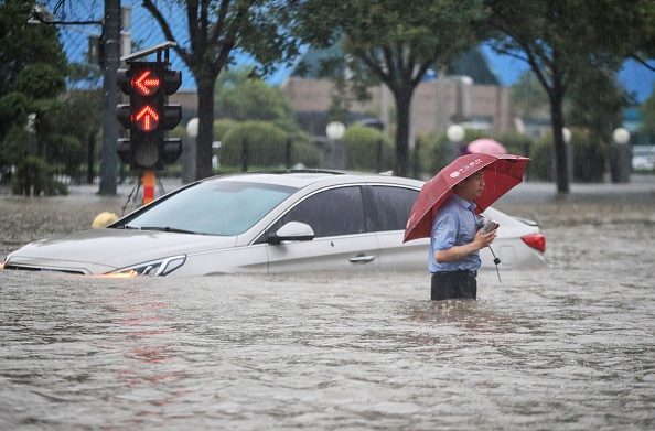 Un homme passe devant une voiture submergée le long d'une rue inondée à la suite de fortes pluies à Zhengzhou, dans la province centrale du Henan en Chine le 20 juillet 2021. (Photo par STR/AFP via Getty Images)