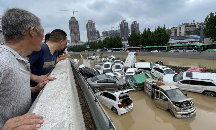 Des gens regardent des voitures baignant dans les eaux de crue après les fortes pluies qui ont frappé la ville de Zhengzhou, dans la province du Henan, en Chine, le 21 juillet 2021. (STR/AFP via Getty Images)