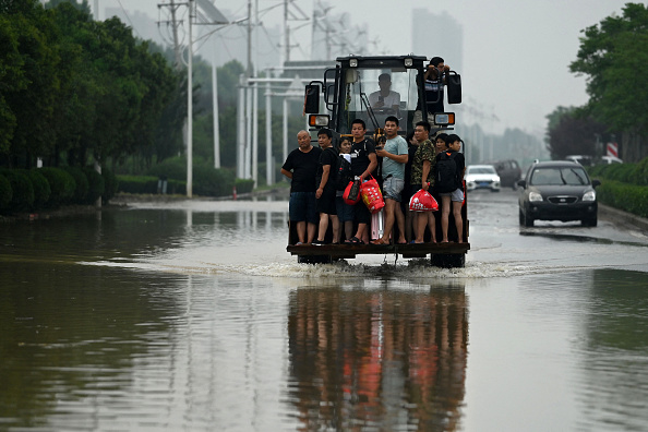 -Des gens roulent à l'avant d’une tractopelle pour traverser une rue inondée à la suite de fortes pluies dans la ville de Zhengzhou, dans le Henan en Chine province le 23 juillet 2021. Photo par NOEL CELIS /AFP via Getty Images.