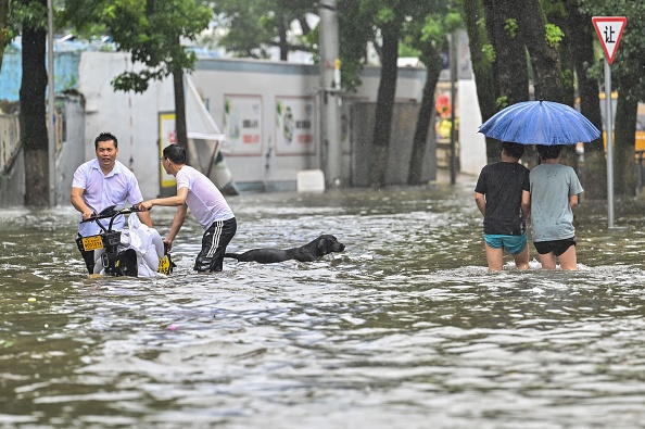 -Des gens pataugent dans une rue inondée de Ningbo, dans la province du Zhejiang le 25 juillet 2021, alors que le typhon In-Fa frappe la côte est de la Chine. Photo par Hector RETAMAL AFP via Getty Images.