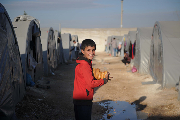 -Illustration- Un garçon réfugié kurde de la ville syrienne de Kobani porte des miches de pain dans sa tente familiale pour le petit-déjeuner. Photo de Kutluhan Cucel/Getty Images.