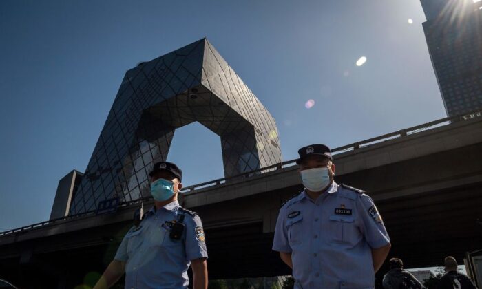 Des policiers portant des masques marchent alors que l'on aperçoit le bâtiment du siège de la télévision centrale chinoise (CCTV) (à gauche, au fond) à Pékin, le 19 mai 2020. (Nicolas Asfouri/AFP via Getty Images)