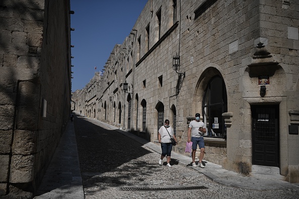 Des touristes masqués marchent dans la « rue des chevaliers » du château médiéval de Rhodes, sur l'île grecque de la mer Égée. (LOUISA GOULIAMAKI/AFP via Getty Images)