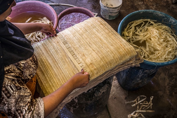 -Une femme étale de fines bandes de papyrus trempées pour former une feuille, avant la compression et le séchage à l'atelier du village dans la région fertile du nord du delta du Nil en Égypte, au nord-est de la capitale, le 28 juillet 2021. Photo de Khaled DESOUKI / AFP via Getty Images.