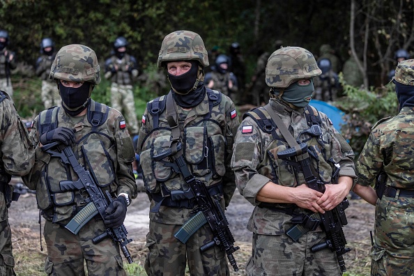 Des soldats et des gardes-frontières polonais se tiennent à côté de migrants présumés originaires d'Afghanistan, près de Bialystok, dans le nord-est de la Pologne, à proximité de la frontière avec le Belarus, le 20 août 2021. (Photo  : RADWANSKI/AFP via Getty Images)