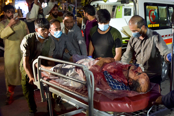 -Des bénévoles et du personnel médical amènent un homme blessé pour qu'il soit soigné après deux puissantes explosions, à l'extérieur de l'aéroport de Kaboul le 26 août 2021. Photo de Wakil KOHSAR / AFP via Getty Images.