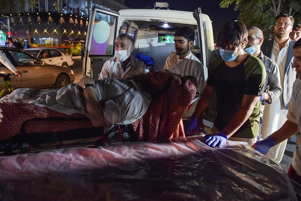 -Des bénévoles et du personnel médical amènent un homme blessé pour qu'il soit soigné après deux puissantes explosions, à l'extérieur de l'aéroport de Kaboul le 26 août 2021. Photo de Wakil KOHSAR / AFP via Getty Images.