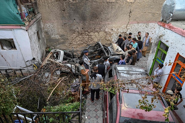 -Des résidents afghans et des membres de la famille des victimes se rassemblent à côté d'un véhicule endommagé à l'intérieur d'une maison, au lendemain d'une frappe aérienne de drones américains à Kaboul le 30 août 2021. Photo de WAKIL KOHSAR/AFP via Getty Images.