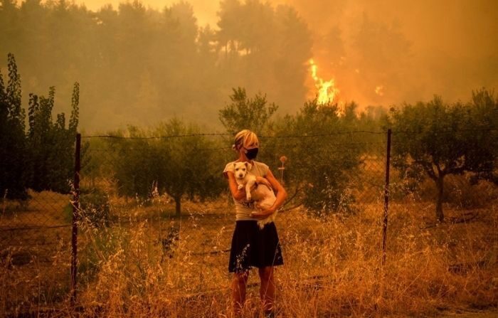 Une femme tient un chien dans ses bras alors que des feux de forêt se rapprochent du village de Pefki sur l'île d'Evia (Eubée), la deuxième plus grande île grecque, le 8 août 2021. (ANGELOS TZORTZINIS/AFP via Getty Images) 