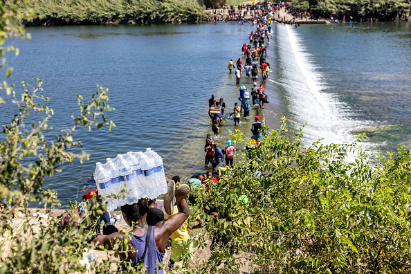 Des migrants traversent à pied le fleuve Rio Grande en transportant de la nourriture et d'autres fournitures vers un campement de fortune situé sous le pont international entre Del Rio, Texas et Acuña, Mexique, le 17 septembre 2021 à Del Rio, Texas.  (Photo : Jordan Vonderhaar/Getty Images)