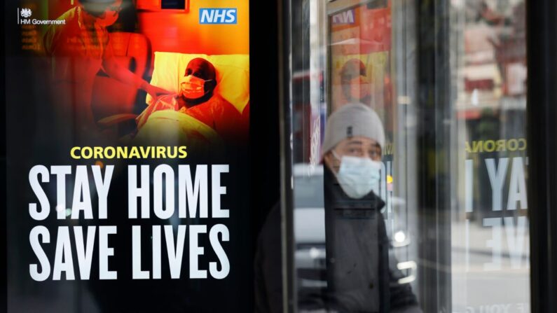 Un passager assis, masqué, dans un abribus où une affiche du NHS rappelle : « Restez chez vous, sauvez des vies », à Chinatown, dans le centre de Londres, le 8 janvier 2021. (Tolga Akmen /AFP via Getty Images)
