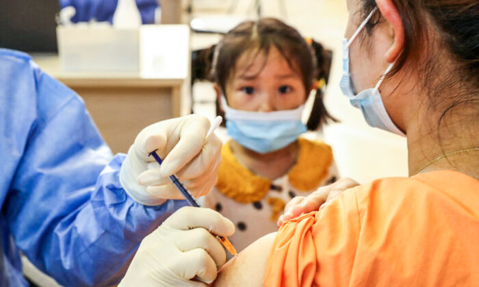 Une fillette regarde une femme se faire vacciner contre le Covid-19 avec le vaccin du groupe China National Biotec (CNBG) à Nantong, dans la province chinoise de Jiangsu (est), le 5 juillet 2021. (STR/AFP via Getty Images)
