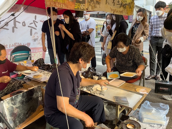 -Les clients font la queue alors que le vendeur de rue Jung Jung-soon et son mari Lim Chang-joo vendent des dalgonas fraîchement préparés, à Séoul le 10 octobre 2021. Photo par Yelim LEE / AFP via Getty Images.