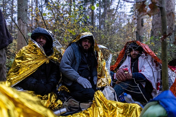 Des migrants syriens s'assoient sous des couvertures de secours pour se protéger de la pluie dans la forêt près de Hajnowka, en Pologne, lors d'une opération de sauvetage conjointe des activistes de "Grupa Granica" (Groupe frontière) et des volontaires de Medycy na Granicy (Médecins à la frontière), le 23 octobre 2021. (Photo : WOJTEK RADWANSKI/AFP via Getty Images)