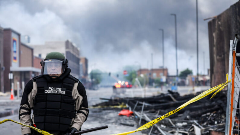 Un officier de police se tient au milieu de la fumée et des débris alors que les bâtiments continuent de brûler après une nuit de manifestations et de violences qui ont suivi la mort de George Floyd, à Minneapolis, le 29 mai 2020. (Charlotte Cuthbertson/The Epoch Times)