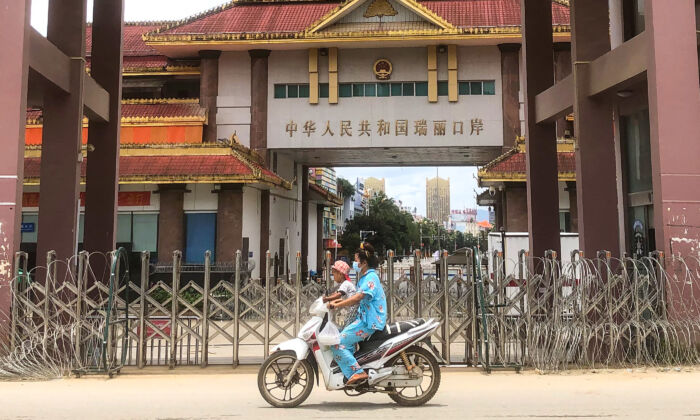 Une femme et un enfant passent en scooter devant la porte frontalière Chine-Myanmar à Muse, en Birmanie, le 5 juillet 2021. (STR/AFP via Getty Images)