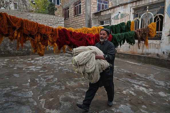 -Un ouvrier marche en tenant des ballots de laine tout en fabriquant des tapis à Herat, le 23 novembre 2021. Photo par Hector RETAMAL / AFP via Getty Images.
