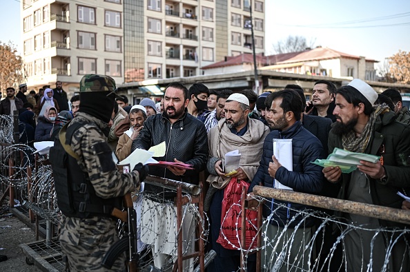 -Un combattant taliban inspecte les documents des personnes faisant la queue pour entrer au bureau des passeports à Kaboul le 18 décembre 2021. Photo de Mohd RASFAN / AFP via Getty Images.
