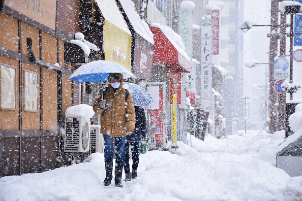 Des gens marchent dans une rue enneigée de la ville de Toyama, provoquée par un front de froid extrême le long de l'ouest et du nord du pays le 27 décembre 2021. Photo de STR/JIJI PRESS/AFP via Getty Images.
