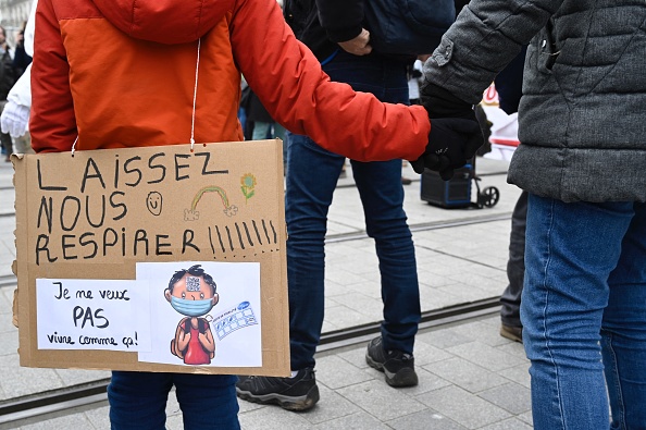 Un adulte tient la main d’un enfant portant une pancarte sur laquelle on peut lire « Laissez-nous respirer » et « Je ne veux pas vivre comme ça » pendant une manifestation contre le pass vaccinal à Nantes le 15 janvier 2022. Crédit : DAMIEN MEYER/AFP via Getty Images.