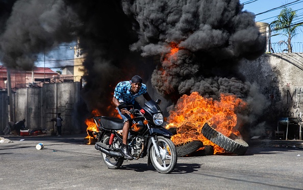 -Un motocycliste passe devant des barricades en feu érigées par des manifestants en réponse à la hausse des prix du carburant, Port-au-Prince, Haïti, 10 décembre 2021. Photo de RICHARD PIERRIN/AFP via Getty Images.