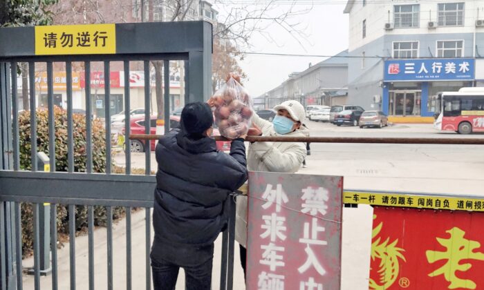 Un habitant reçoit de la nourriture à l'entrée d'une zone résidentielle fermée et restreinte en raison d'une épidémie de Covid-19 à Anyang, dans la province du Henan, le 12 janvier 2022. (STR/AFP via Getty Images)