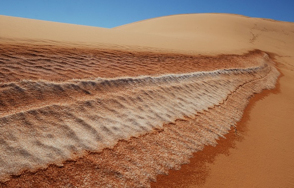 Image d'illustration : de la neige sur les dunes de sables d'un désert. (MARK RALSTON/AFP via Getty Images)