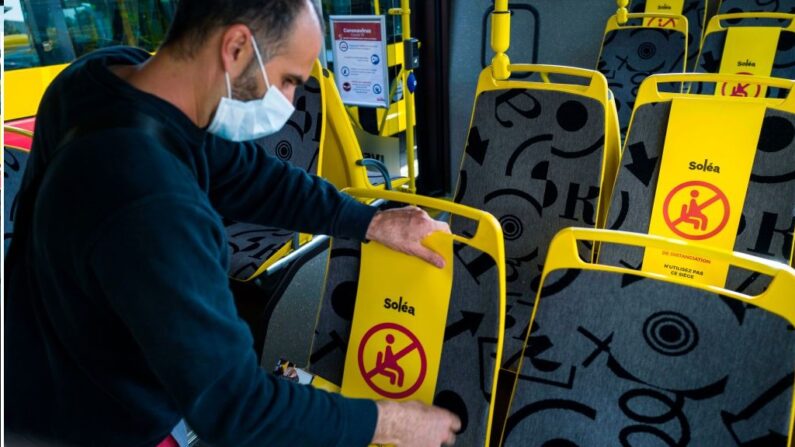 Un employé portant un masque de protection installe un autocollant indiquant les règles de distanciation sociale requises, sur les sièges d'un bus Solea à Mulhouse, dans l'est de la France, le 8 mai 2020. (Photo par SEBASTIEN BOZON/AFP via Getty Images)
