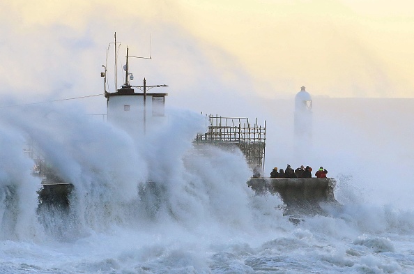 Les gens regardent les vagues s'écraser contre la digue à Porthcawl, dans le sud du Pays de Galles, le 18 février 2022, la tempête Eunice apporte des vents violents à travers le pays. Photo de Geoff CADDICK/AFP via Getty Images.