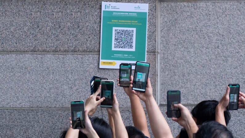 Alors qu'ils font la queue pour entrer dans la foire annuelle du livre de Hong Kong, les visiteurs scannent un code QR pour l'application "Sortir de la maison sans risque" imposée par le gouvernement afin de tracer les personnes positives au Covid-19, le 17 juillet 2021, Hong Kong (Photo par BERTHA WANG/AFP via Getty Images)