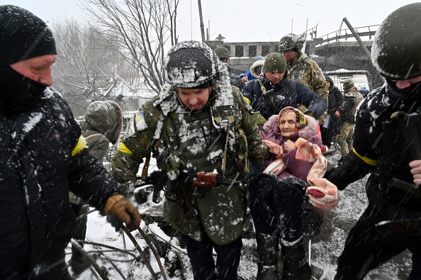 -Des soldats ukrainiens aident une femme âgée à traverser un pont détruit alors qu'elle évacue la ville d'Irpin, au nord-ouest de Kiev, le 8 mars 2022. Photo SERGEI SUPINSKY/AFP via Getty Images.