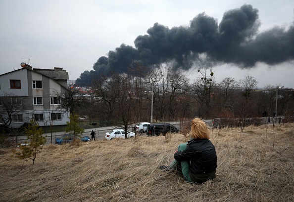 Une jeune femme est assise au sommet d'une colline et regarde la fumée noire et les flammes s'élever d'un incendie à la suite d'une frappe aérienne dans la ville de Lviv, dans l'ouest de l'Ukraine, le 26 mars 2022. Photo ALEKSEY FILIPPOV/AFP via Getty Images.