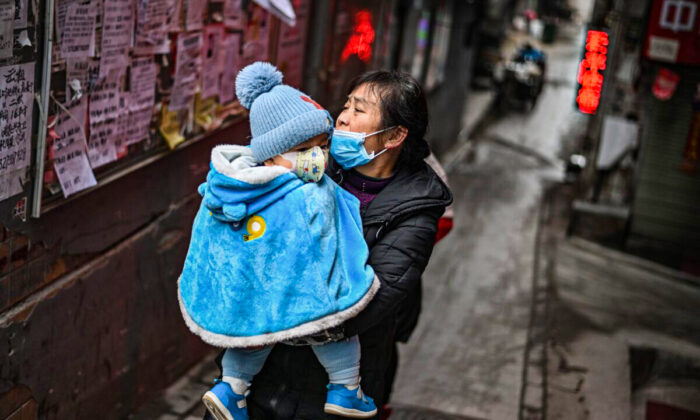 Une femme avec un masque facial tient son bébé dans ses bras à Wuhan, dans le Hubei, le 22 janvier 2021. (Photo par HECTOR RETAMAL/AFP via Getty Images)