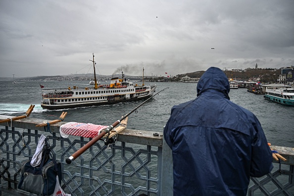 Un homme à côté de sa canne à pêche sur le pont de Galata un jour de pluie alors qu'un ferry tente d'accoster au port, à Istanbul, le 4 décembre 2019. Photo par OZAN KOSE/AFP via Getty Images.