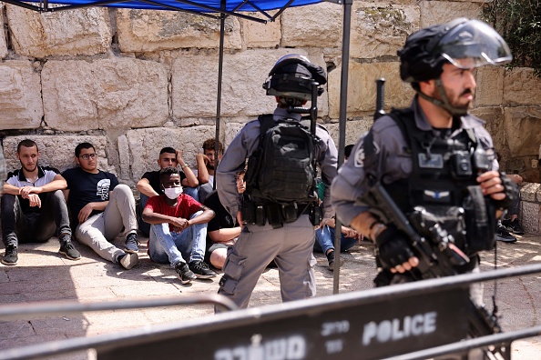 Les forces de sécurité israéliennes montent la garde à côté de Palestiniens détenus à l'entrée de l'enceinte de la mosquée de Jérusalem, le 21 mai 2021, après de nouveaux affrontements entre Palestiniens et la police israélienne. Photo de Menahem KAHANA / AFP via Getty Images.