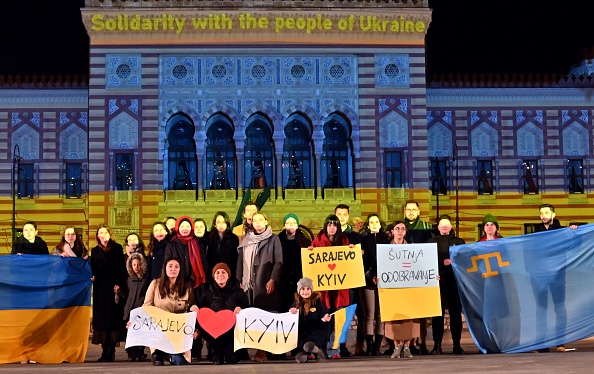 Un petit groupe de citoyens se rassemble devant l'hôtel de ville de Sarajevo illuminé aux couleurs du drapeau ukrainien, le 24 février 2022. Photo par ELVIS BARUKCIC/AFP via Getty Images.