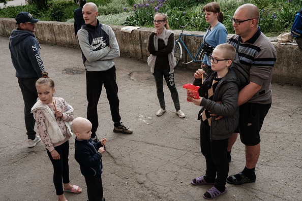 Vladyslav Sheremet, 30 ans, tient son fils de 9 ans alors, sa famille et d'autres ont décidé de ne pas évacuer, se rassemblent à l'extérieur de leur abri au sous-sol à Lysychansk, dans l'est de l'Ukraine, le 15 mai 2022.  Photo de YASUYOSHI CHIBA/AFP via Getty Images.