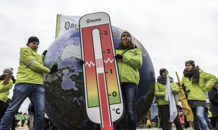 Une femme tient un thermomètre géant devant une maquette de la Terre lors de la Marche mondiale pour le climat à Berlin, en Allemagne, le 29 novembre 2015. (Carsten Koall/Getty Images)