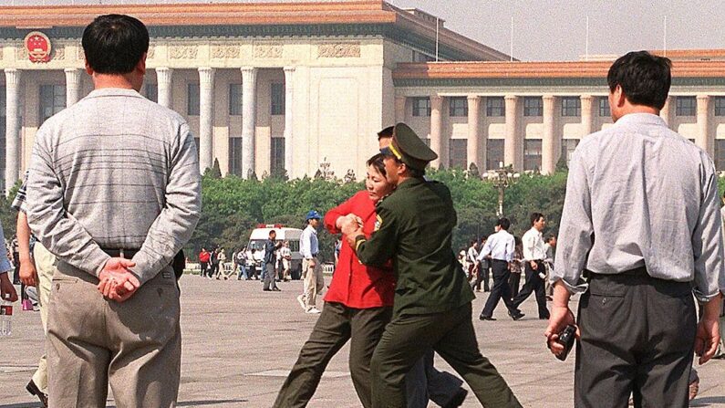 Des policiers en civil observent une pratiquante de Falungong qui résiste à son arrestation alors qu'elle est forcée par la police à se diriger vers un fourgon de police, le 11 mai 2000 sur la place Tiananmen à Pékin.(STEPHEN SHAVER/AFP via Getty Images)
